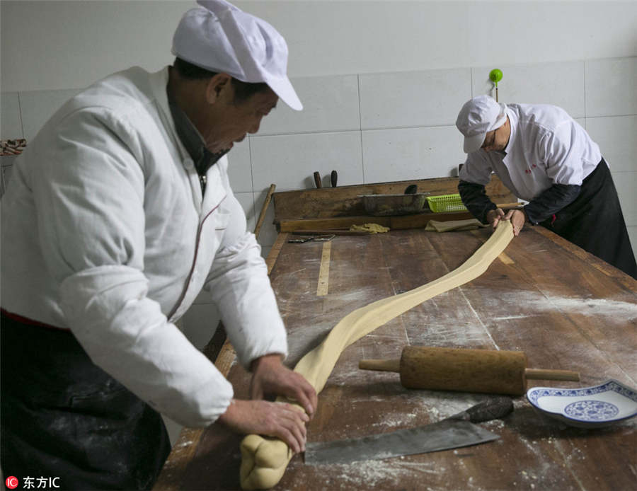 Maestros dulceros estiran la masa, antes de cortarla en fragmentos en forma de moneda.