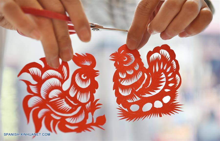 Imagen del 29 de diciembre de 2016 de Chang Yangyang, un joven artista folclórico, mostrando sus trabajos de papel cortado de un gallo y una gallina, en el condado de Mengjin, provincia de Henan, en el centro de China. Los chinos celebrarán el A?o Nuevo Lunar, o Festival de Primavera, el 28 de enero de 2017. El Festival de Primavera esta vez marca el comienzo del A?o del Gallo, de acuerdo con el zodíaco chino que asigna uno de los 12 animales a cada a?o. (Xinhua/Huang Zhengwei)