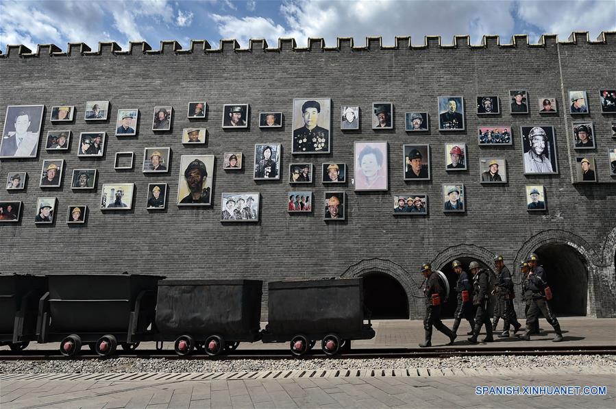 Mineros caminan frente a una pared con fotografías en el Parque Minero Nacional de Jinhuagong, en la ciudad de Datong, en la provincia de Shanxi, en el norte de China, el 16 de mayo de 2017. (Xinhua/Cao Yang)