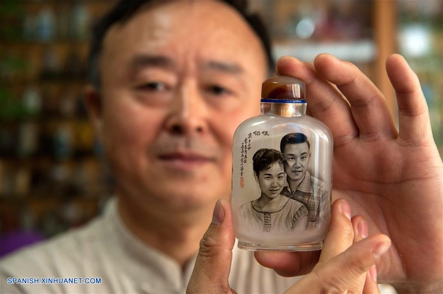 Imagen del 20 de julio de 2017 de Dong Xue, un artista de pintura interior, mostrando una botella de vidrio de tabaco pintada en el interior, en su vivienda en Shijiazhuang, capital de la provincia de Hebei, en el norte de China. La botella de tabaco de vidrio pintada en el interior es una artesanía tradicional china. El arte de pintura interior, que tiene una historia de más de 200 a?os, fue inscrita también como uno de los patrimonios culturales nacionales intangibles. Dong Xue y su hija han continuado estudiando la técnica y decidieron transmitirla. (Xinhua/Pu Dongfeng)