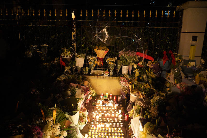 Flores y velas depositadas en la acera de una calle cercana a la Escuela Primaria de Lenguas Extranjeras de Shanghai, como tributo a las víctimas de un ataque con cuchillo que dejó a dos estudiantes muertos y a un estudiante y una se?ora heridos. [Foto: Gao Erqiang]