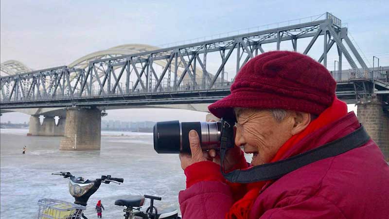 Zhang Ying, de 93 a?os, toma fotos con su mini cámara digital a la orilla del río Songhua en Harbin, capital de la provincia de Heilongjiang, 14 de diciembre del 2018. [Foto: Wang Kun/ Chinadaily.com.cn]