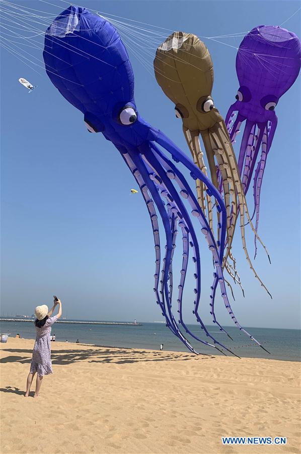 WEIFANG, 1 mayo, 2020 (Xinhua) -- Una mujer toma fotografías de cometas volando en una playa durante el primero de los cinco días de vacaciones públicas, en Weifang, en la provincia de Shandong, en el este de China, el 1 de mayo de 2020. (Xinhua/Str)