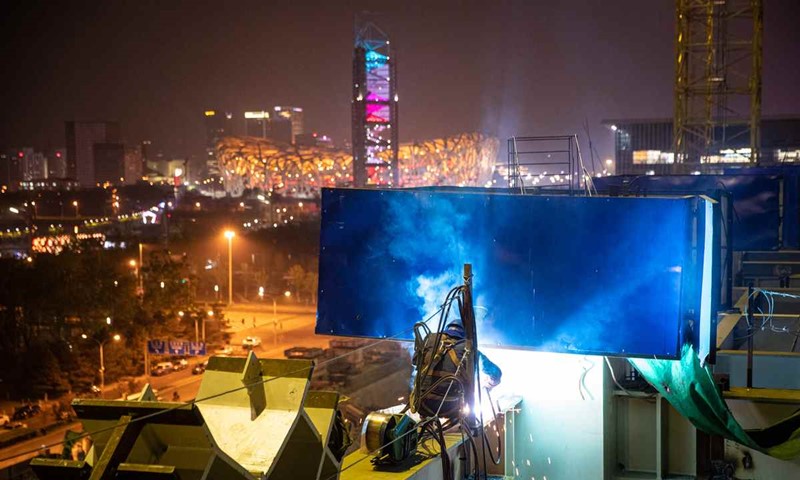 Un soldador trabaja en la azotea de acero del Centro Nacional de Convenciones de Beijing el 14 de abril, con el Nido de Pájaro en el fondo. El trabajo de construcción es la segunda fase de un proyecto para expandir el centro de convenciones. [Foto por Kuang Linhua / China Daily]