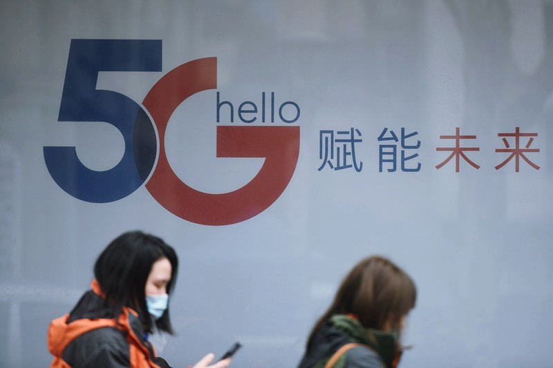 Esta foto del 26 de enero de 2021 muestra varios pasajeros frente al logotipo de 5G en la ciudad de Hangzhou (en la provincia de Zhejiang, este de China). (Long Wei / Pueblo en Línea)